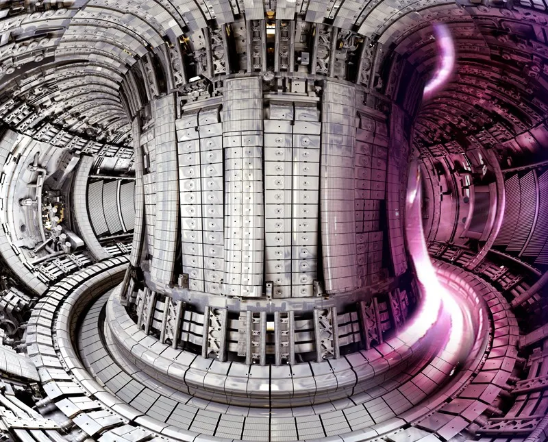 Interior of a tokamak fusion reactor: a doughnut-shaped chamber lined with metal tiles, with glowing pink plasma overlaid on the right side.